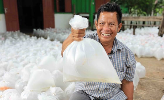 A farmer in Lao holds up a bag of fresh fish that he has cultivated in his rice field.