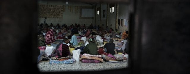 Migrants sit on mattresses laid on the floor at a detention centre located in Libya. Migrants sit on mattresses laid on the floor at a detention centre located in Libya.